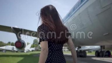 快乐顽皮的黑发女孩戴着太阳镜在大飞机前旋转，看着相机。 夏天。 快乐